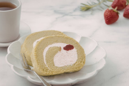 A green matcha cake roll with pink filling and a red strawberry on top, served on a white plate with...