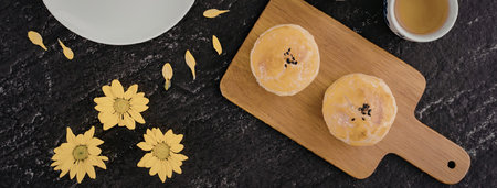 Two orange-colored pastries on a wooden cutting board with yellow flowers and a cup of tea