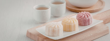 A plate of assorted mooncakes on a wooden cutting board with cups of tea