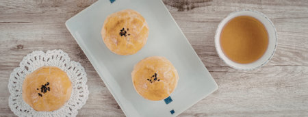 A photo of two pastries on a plate and a cup of tea on a wooden table.
