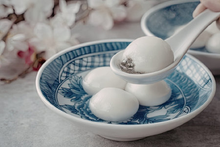 A bowl of tangyuan, small white rice balls served in a blue and white bowl with a spoon holding one...