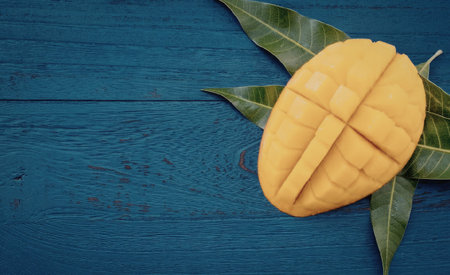 A vibrant yellow mango cut into slices on a blue wooden surface with green leaves.