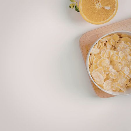 A bowl of corn flakes on a wooden cutting board with a halved orange
