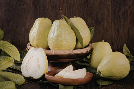 A still life of green guavas in a woven basket with some sliced and scattered around, set against a...