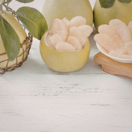 A still life of pomelos with some sliced open to reveal the segments, on a white wooden surface.の写真素材
