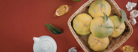 A woven basket filled with fresh green oranges, accompanied by a few leaves and scattered around on...