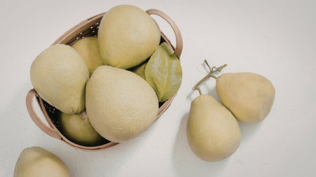 A woven basket filled with fresh pears, accompanied by a few loose pears on a white surface.