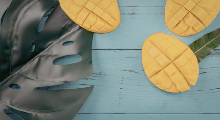 A vibrant image of sliced mangoes arranged on a light blue wooden surface, accompanied by large green leaves, evoking a sense of tropical freshness and summer delight.の写真素材