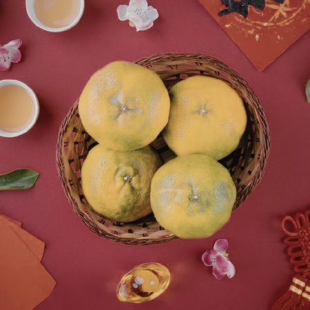 A woven basket filled with four vibrant green and orange orbs, likely oranges or tangerines, surrounded by festive decorations and cups of tea on a red background.の写真素材
