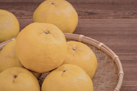 A close-up of several vibrant oranges arranged in a traditional woven basket on a wooden surface.