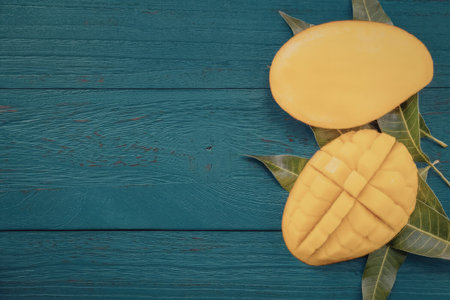 A sliced and whole mango with green leaves on a blue wooden surface