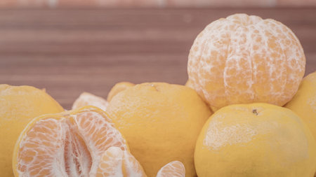 A vibrant display of fresh oranges and peeled mandarin on a wooden surface, showcasing their bright...