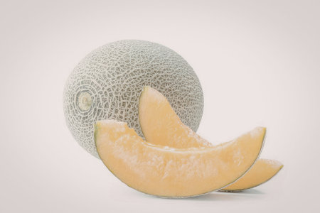 A whole cantaloupe with two slices in front on a plain white background