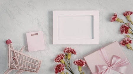 A pink gift box with a ribbon, a white picture frame, pink flowers, and a small pink shopping cart...