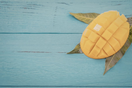A vibrant yellow mango cut into a grid pattern on a light blue wooden surface with green leaves