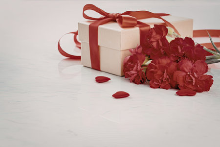 A beautifully wrapped gift box adorned with a red ribbon and accompanied by a bouquet of vibrant red...