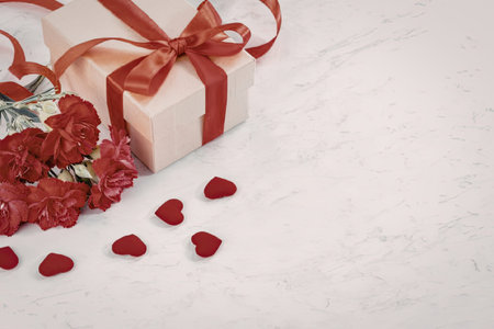A gift box wrapped with a red ribbon and surrounded by red heart-shaped confetti.