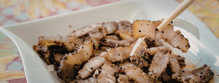 A white plate filled with grilled meat, possibly pork or chicken, with a pair of chopsticks picking...