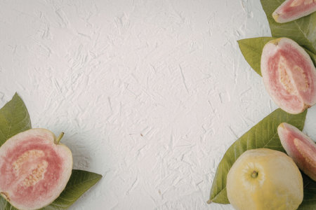 An image of guava fruit slices and leaves arranged on a white textured surface, showcasing the pink...