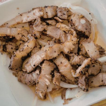 A plate of grilled pork belly with sliced onions, seasoned with herbs and spices.