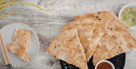 A plate of sliced naan bread served with dipping sauce and herbs