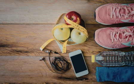 A smartphone, earbuds, pink sneakers, a water bottle, and a dumbbell on a wooden floor