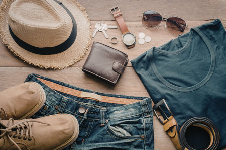 A collection of casual clothing and accessories arranged on a wooden surface, including a hat,...