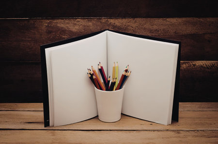 An open book with a cup of colored pencils on a wooden table
