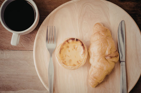 A breakfast plate with a croissant, quiche and a cup of coffee on a wooden table.
