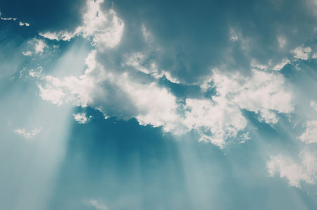 A serene blue sky with white clouds and sunlight rays shining through