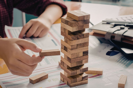 A person playing with wooden blocks, likely a game of Jenga, on a desk with papers and office...