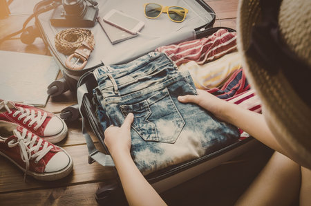 a person packing a suitcase with various clothing items and accessoriesの写真素材