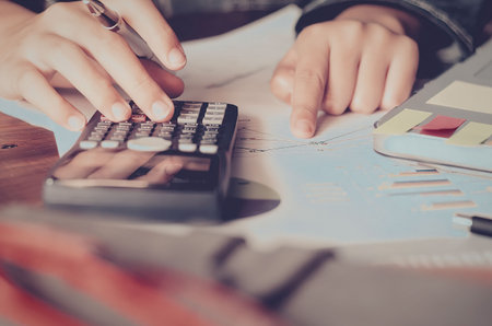 A person using a calculator on a desk with financial documents and papers.