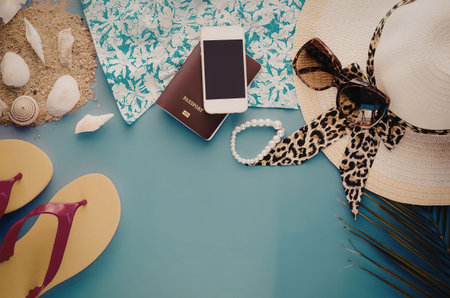 A collection of summer vacation items including a hat, flip flops, phone, and more on a blue...