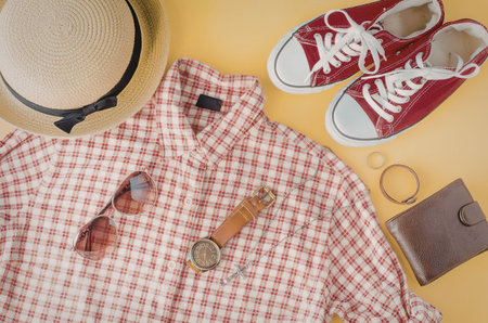 A neatly arranged flat lay of a casual summer outfit consisting of a red and white gingham shirt,...