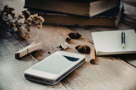 A smartphone, notebook, pen, and other office supplies on a wooden desk.