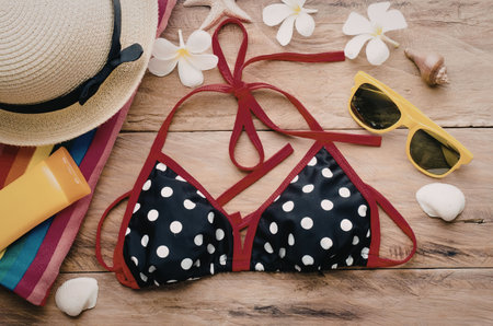 A black and white polka dot bikini top with red trim and straps, surrounded by summer accessories...