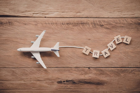 A white airplane model on a wooden surface with travel tiles arranged to spell 'travel'.