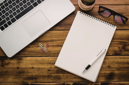 A laptop, notebook, pen, glasses, and coffee on a wooden deskの写真素材