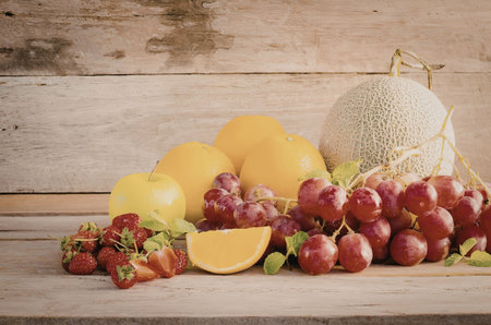A colorful arrangement of fresh fruits on a wooden table, including strawberries, grapes, orange,...