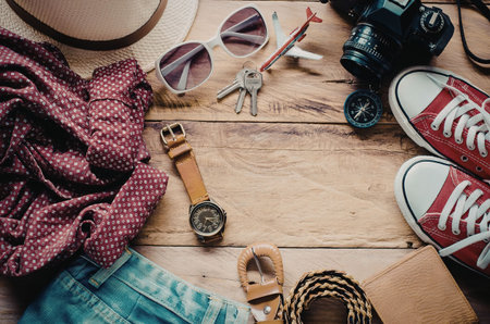 A collection of travel items including clothing, accessories, and gadgets laid out on a wooden...