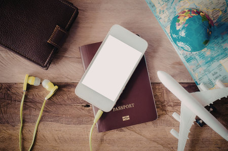 A collection of travel essentials including a phone, passport, earbuds, wallet, and airplane model...
