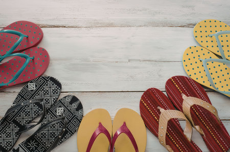 A collection of vibrant flip flops in various colors and patterns, arranged on a rustic wooden...