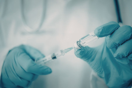 A medical professional wearing blue gloves holding a syringe and a vial of vaccine, emphasizing...
