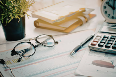 A cluttered desk with office supplies, financial documents, and a calculator.の写真素材
