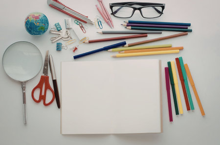 A collection of school supplies including a notebook, pencils, pens, crayons, scissors, magnifying...