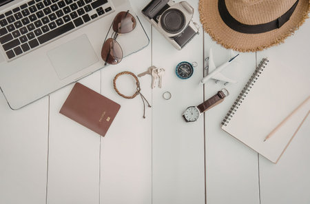 A collection of travel essentials including a laptop, camera, hat, notebook, watch, and accessories...