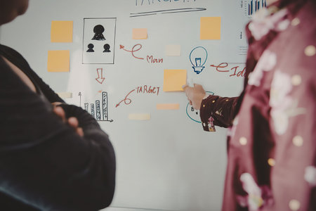 Two individuals engaged in planning a project using sticky notes on a whiteboard