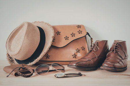 A still life of travel accessories including a straw hat, sunglasses, scarf, leather bag, and brown...