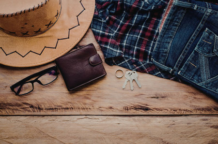 A still life composition featuring a rustic western lifestyle with a hat, wallet, glasses, keys, and...